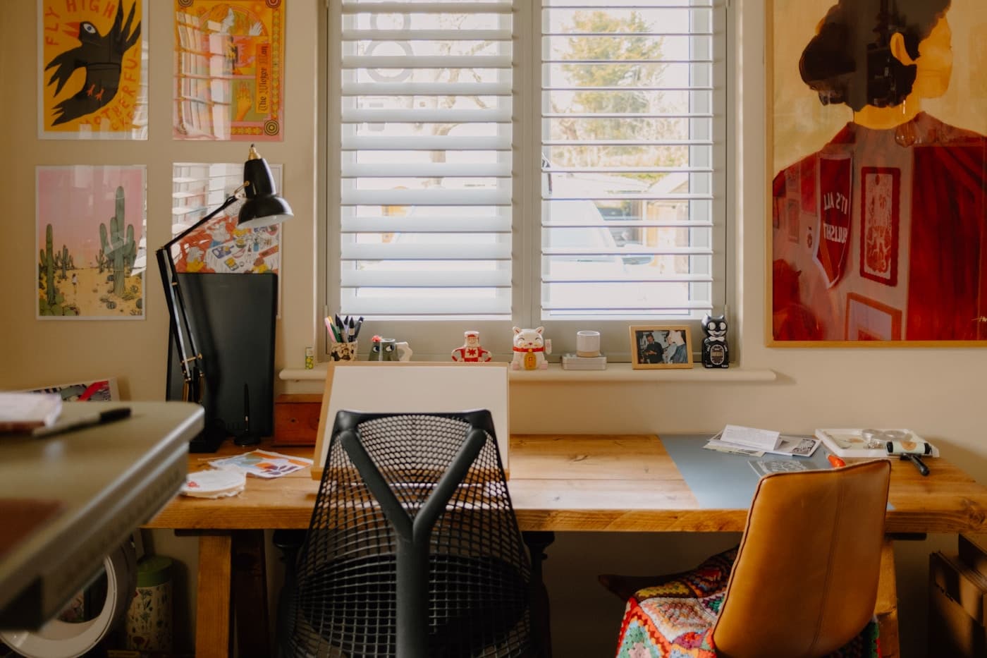 A creative's studio desk surrounded by art prints in warm window light.